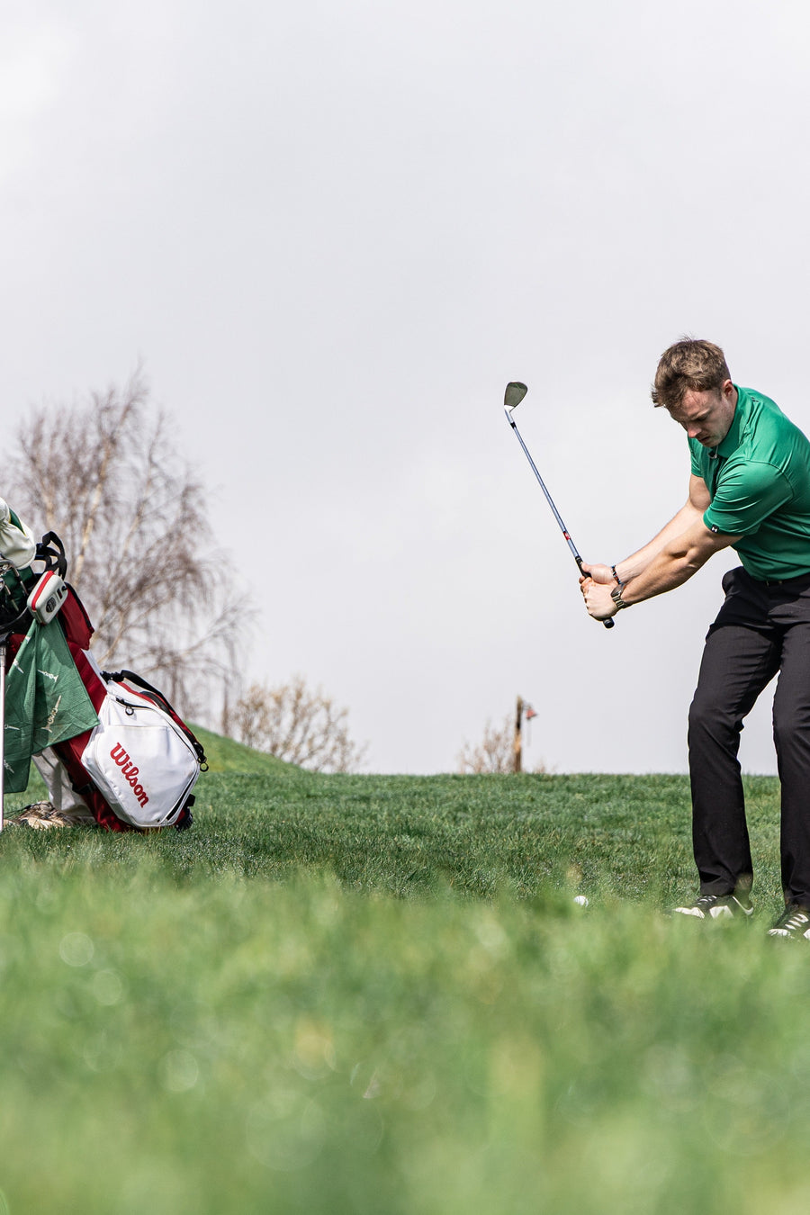 Man swinging a golf club on a golf course with a bag in the background